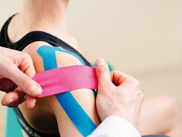 doctor applying pink and blue tape to shoulder